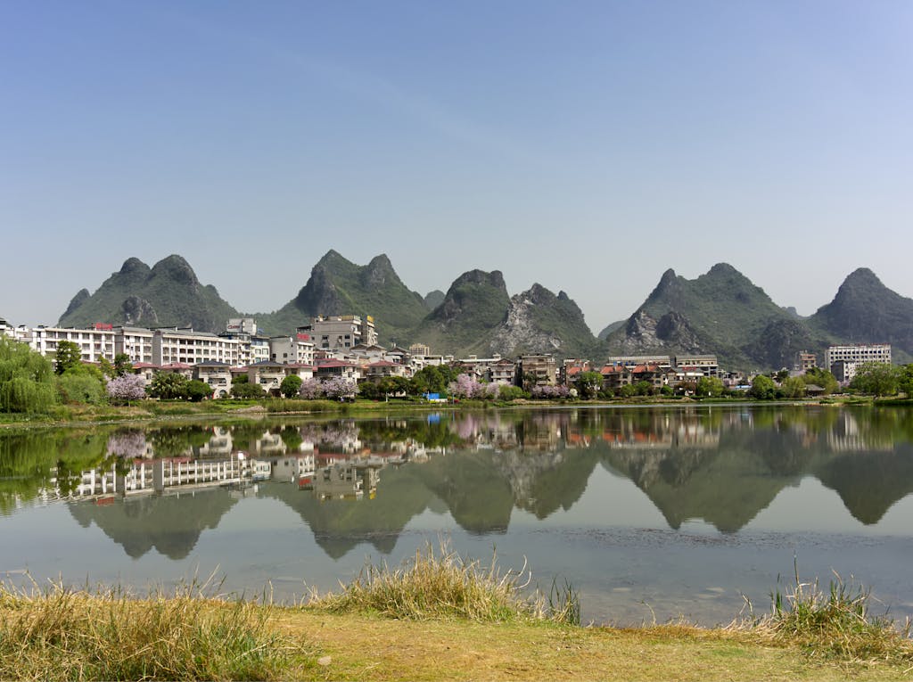 Scenic view of karst hills reflecting in a lake surrounded by buildings and greenery.