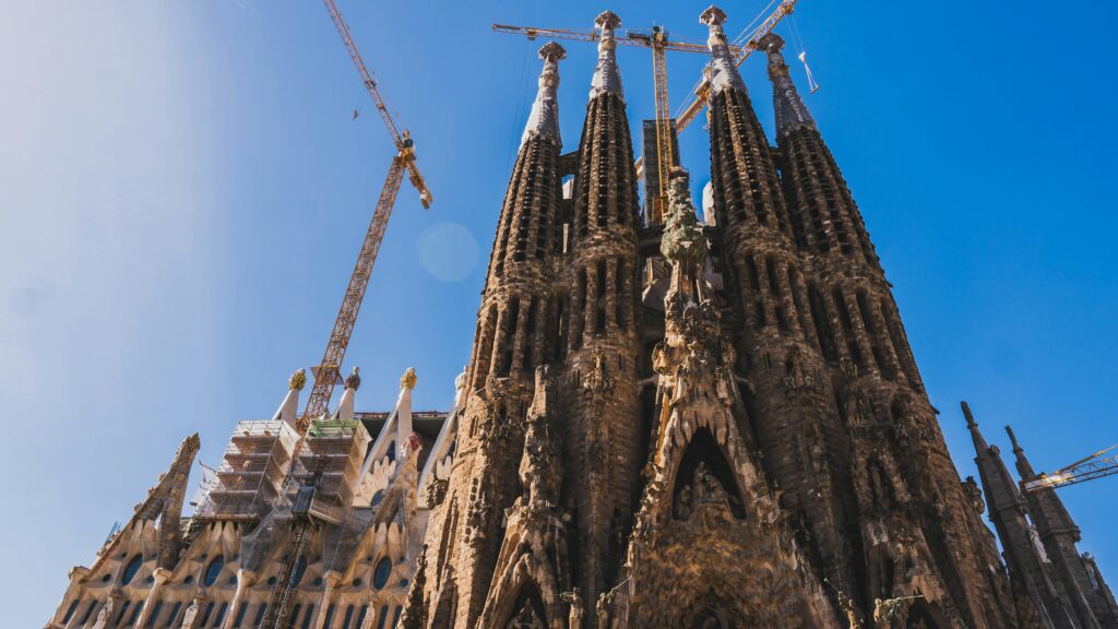 View of Sagrada Familia's intricate facade and cranes against a clear blue sky in Barcelona.